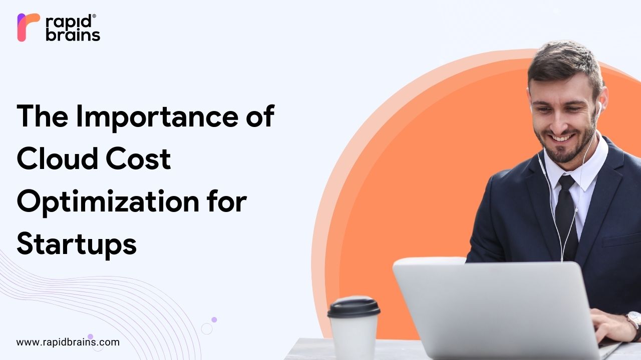 A smiling businessman in a suit and earphones working on a laptop, with a coffee cup beside him. Text on the image reads: "The Importance of Cloud Cost Optimization for Startups" with the RapidBrains logo and website URL (www.rapidbrains.com).